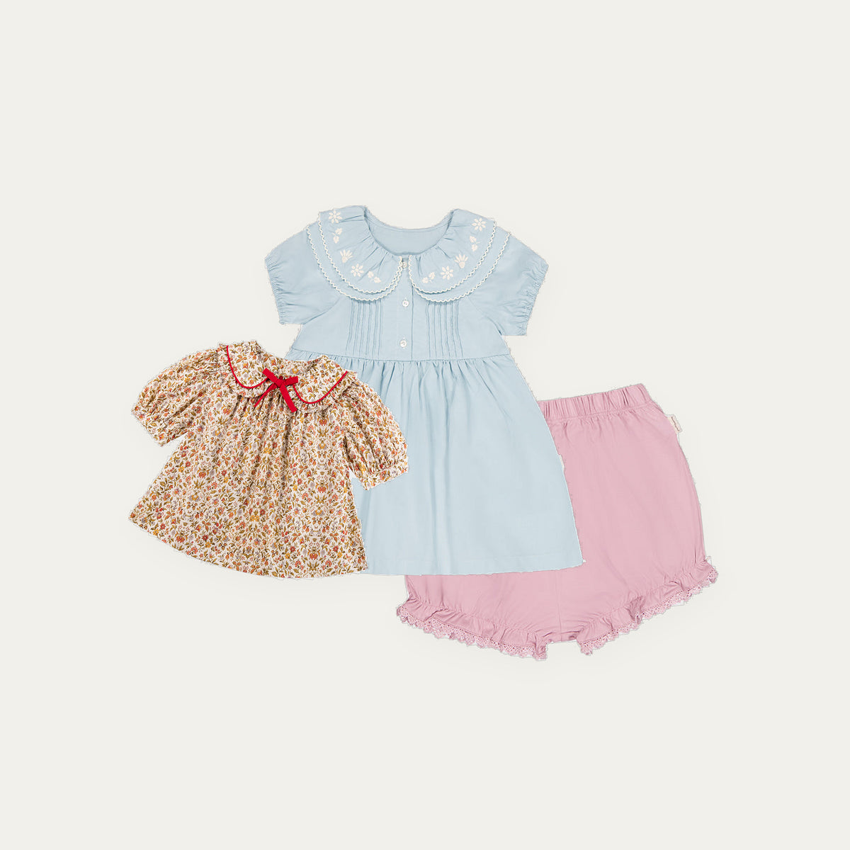 Happyology Lucky Bag, three spring summer sample pieces laid out - blue pintuck dress, floral blouse and frilled bloomers